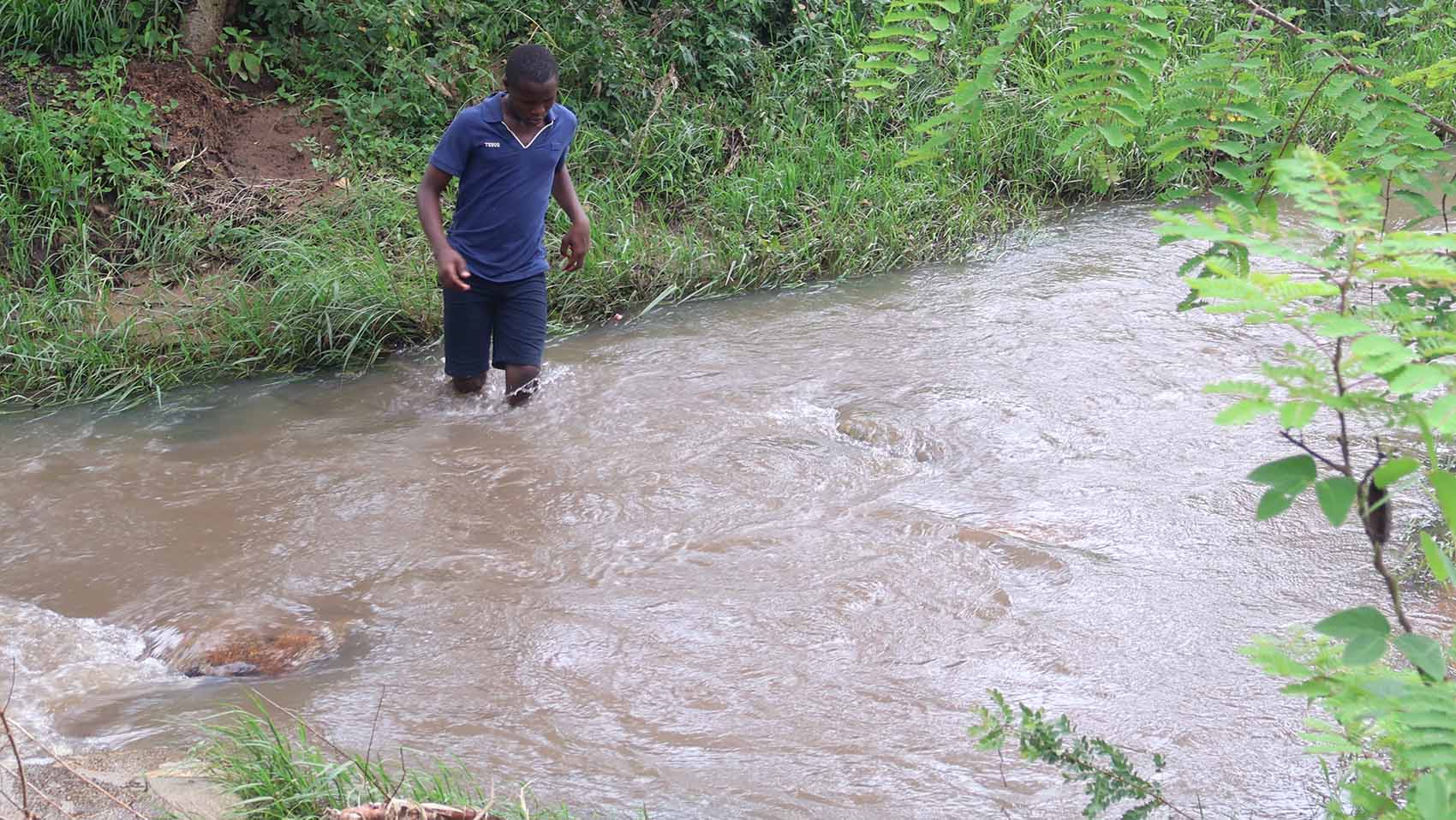 A boy crosses the river where there was once a makeshift bridge.